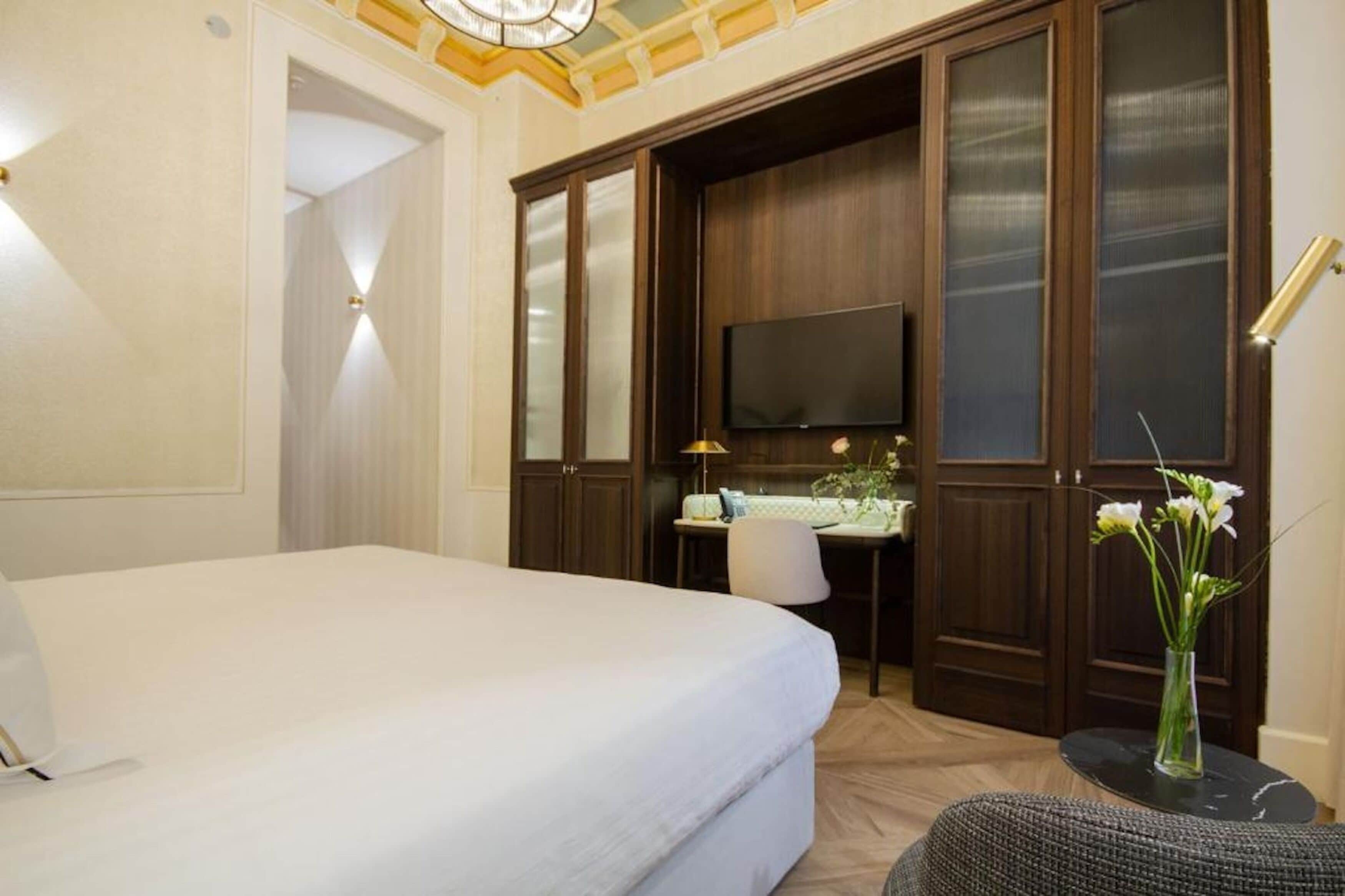 Habitación de hotel con una cama grande, un escritorio con silla, un televisor y un florero con flores.