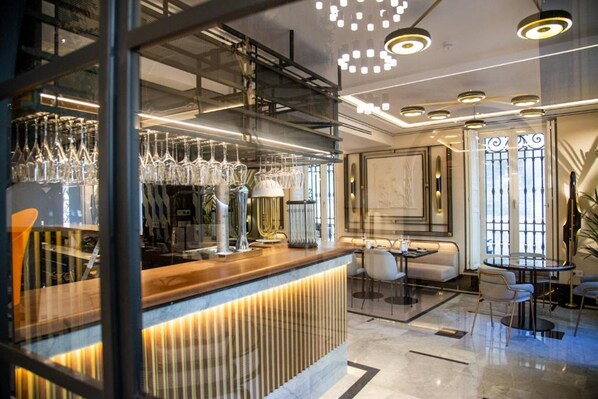 Zona de bar moderna con mostrador de madera, copas y diferentes disposiciones de asientos.