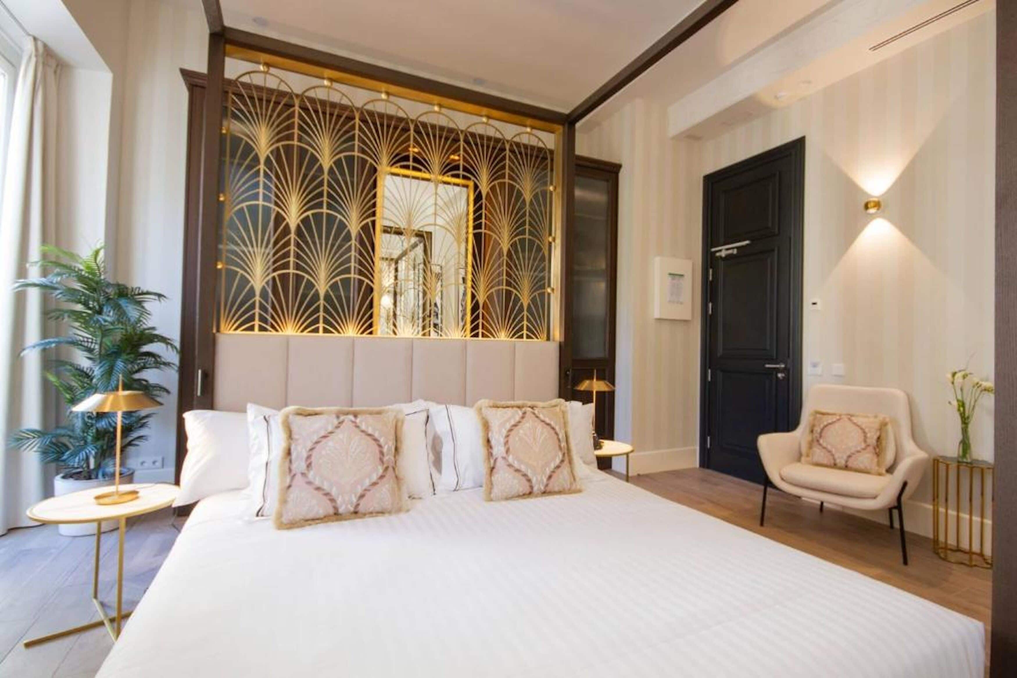 A modern hotel room with a large bed, a decorative screen, a sitting area with a chair, and a door.