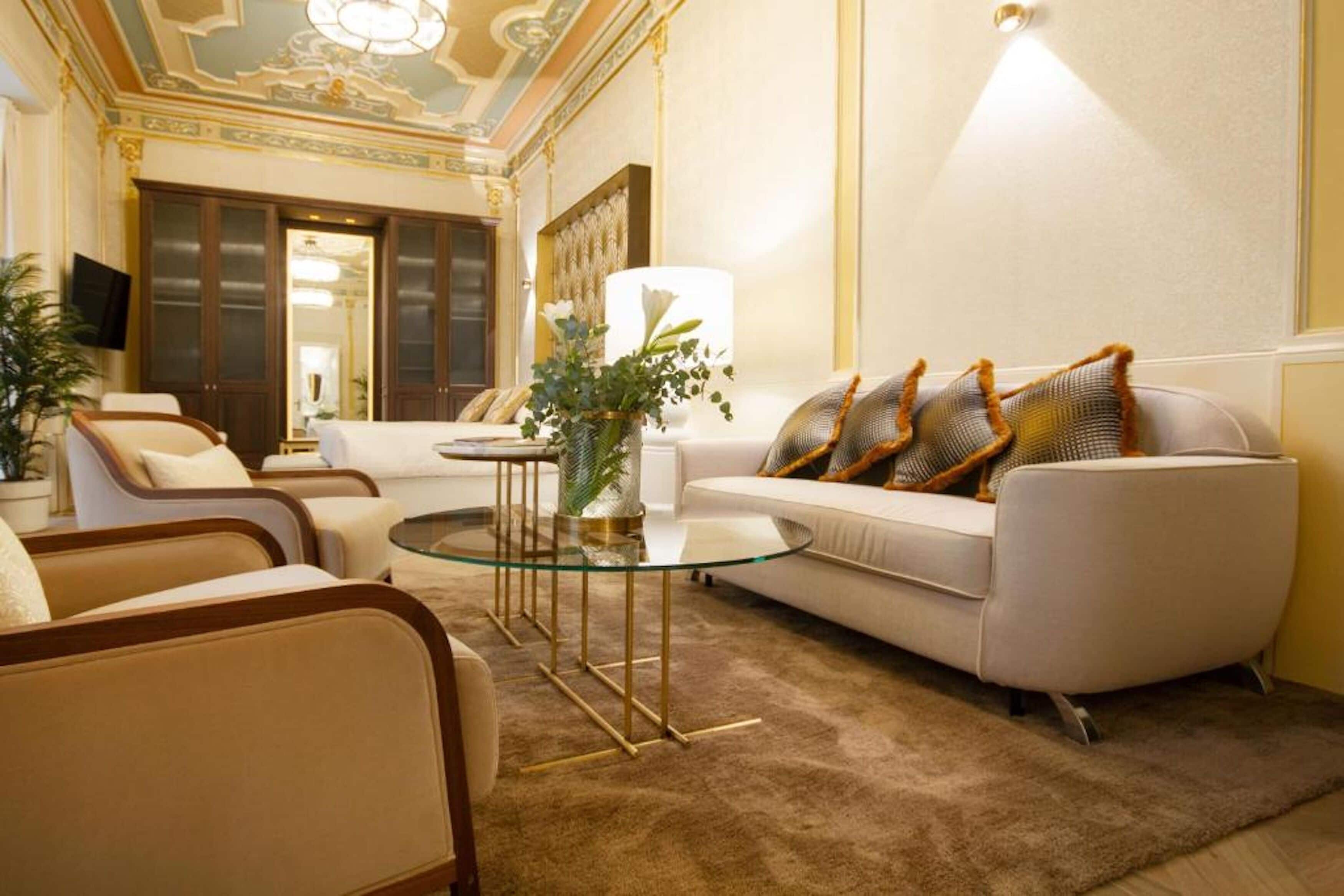 Un salon luxueux comprenant un canapé, des fauteuils, une table basse en verre et un vase décoratif.