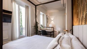 A hotel room with a large bed, a desk with a chair, a TV, and a balcony with curtains.