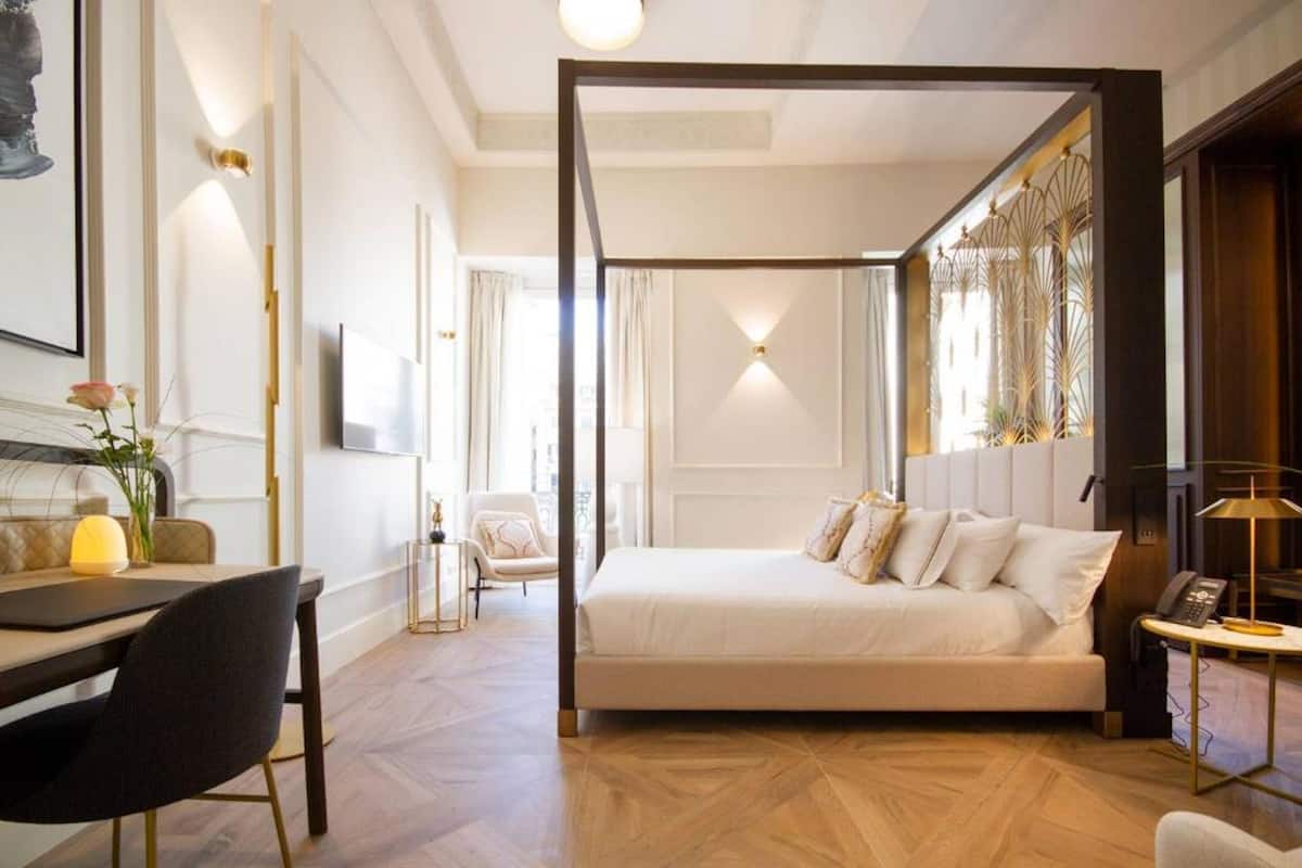 A bedroom with a large bed, a desk with a chair, a TV, and a window with curtains.