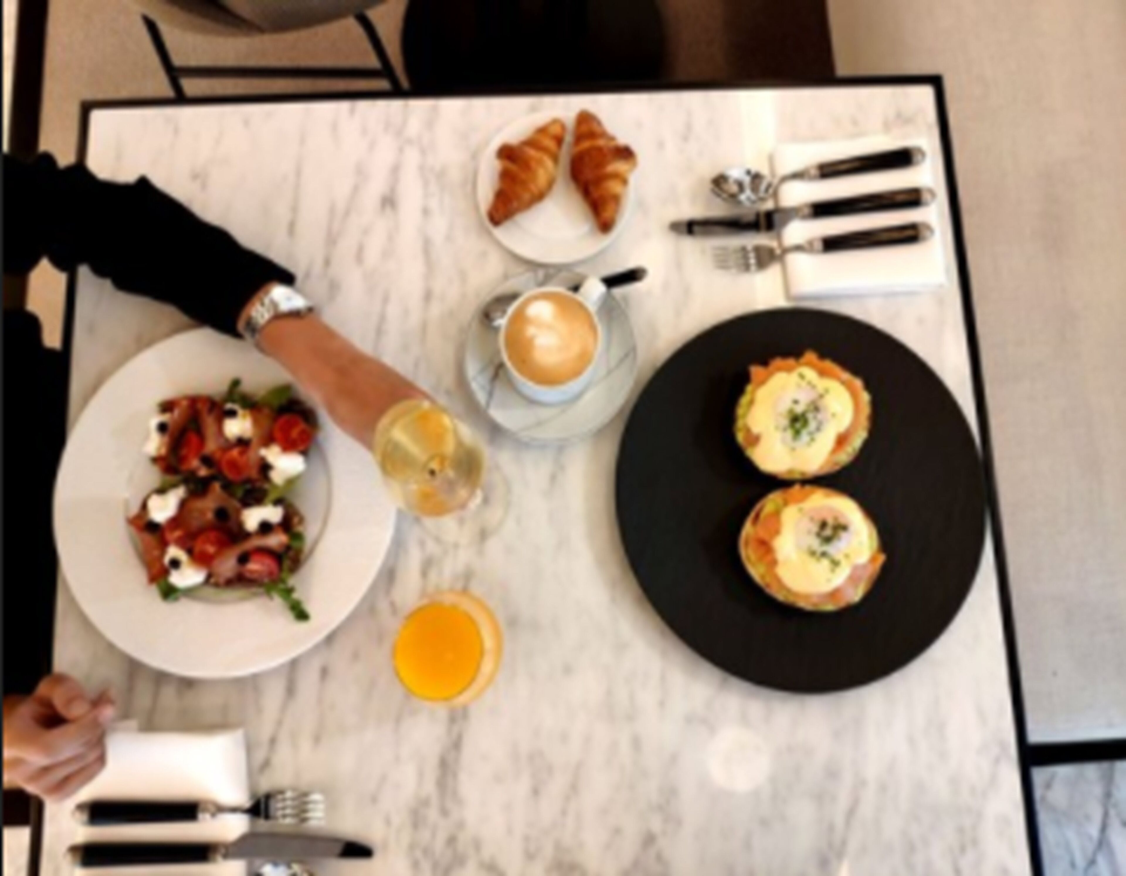 A breakfast setting with croissants, a plate of eggs, and a glass of orange juice on a marble table.