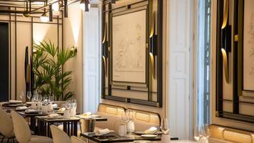 A dining area with tables set for a meal, a large plant, and a wall with a decorative relief.
