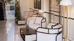 A modern lobby with a seating area featuring sofas and a coffee table, a large floor lamp, and a decorative plant. - MYR Palacio Vallier (Valencia)
