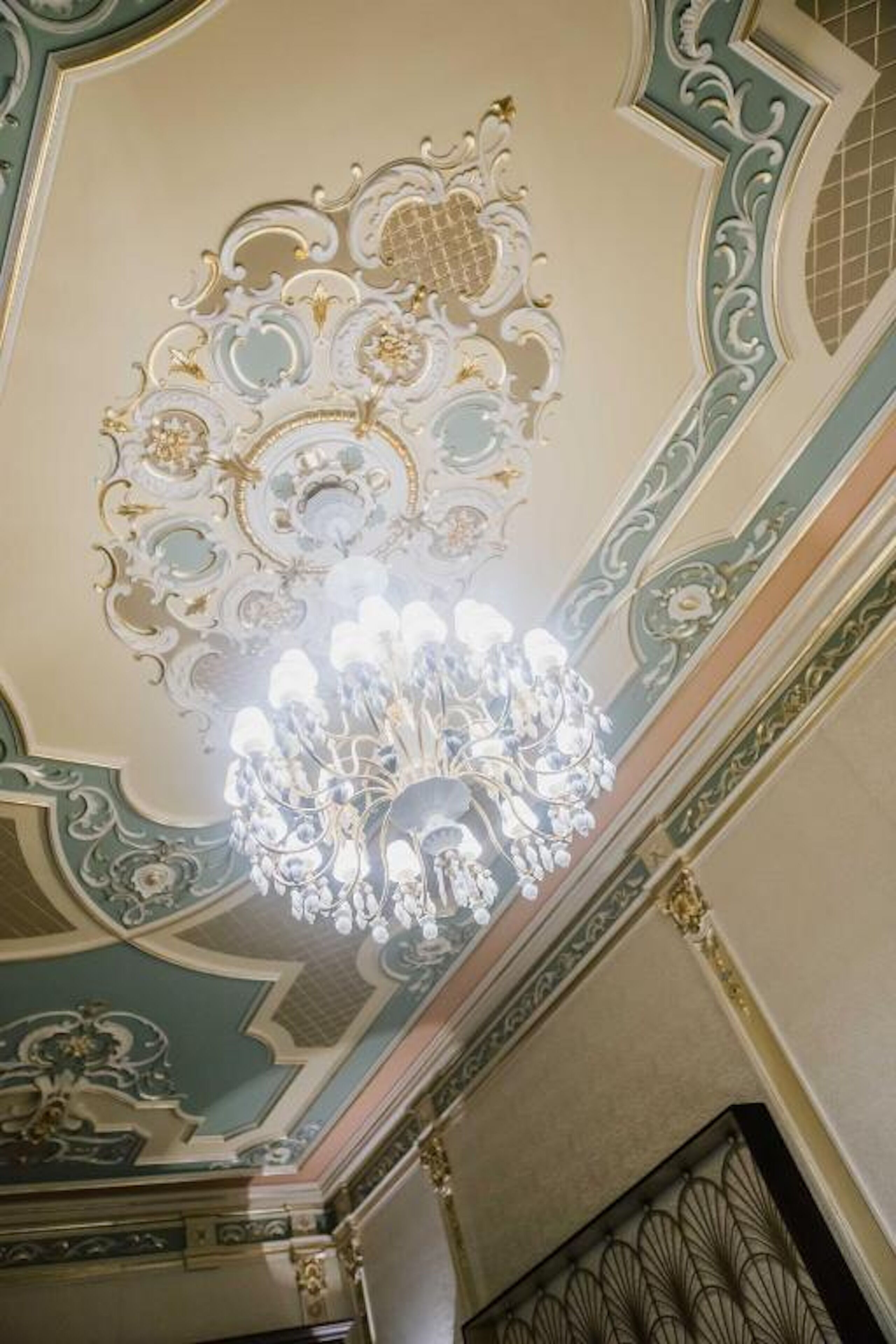 A ceiling with ornate gold and white decorations, a chandelier, and a geometric pattern.