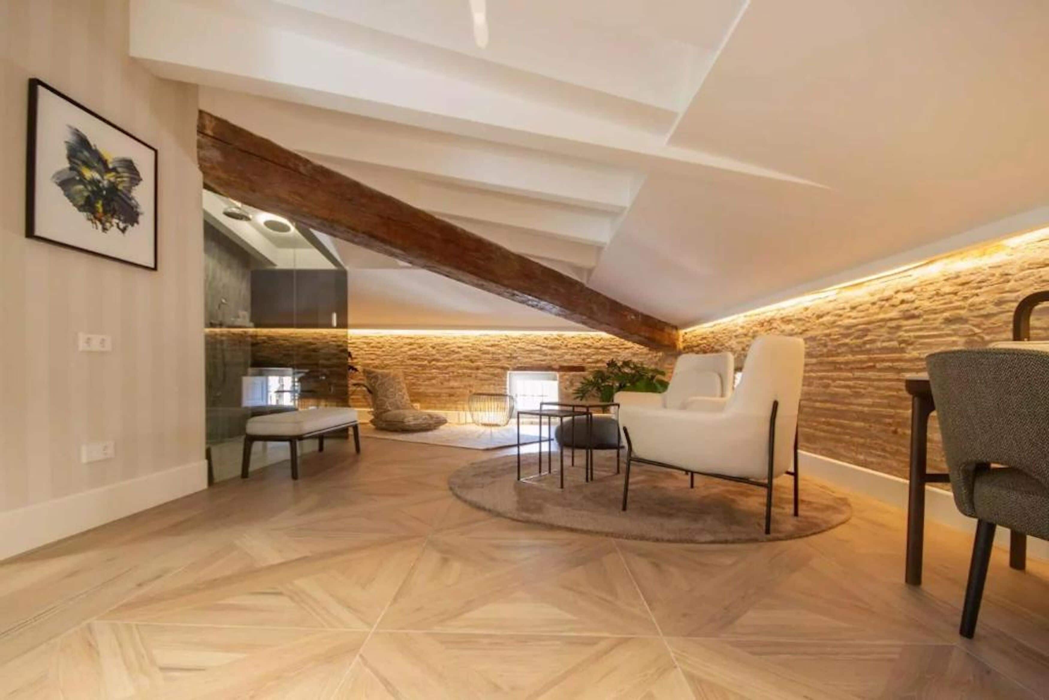 A modern loft with exposed wooden beams, a stone accent wall, and a cozy seating area with a round rug.