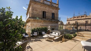 A rooftop terrace with outdoor seating, a stone building, and a clear blue sky. - MYR Palacio Vallier (Valencia)