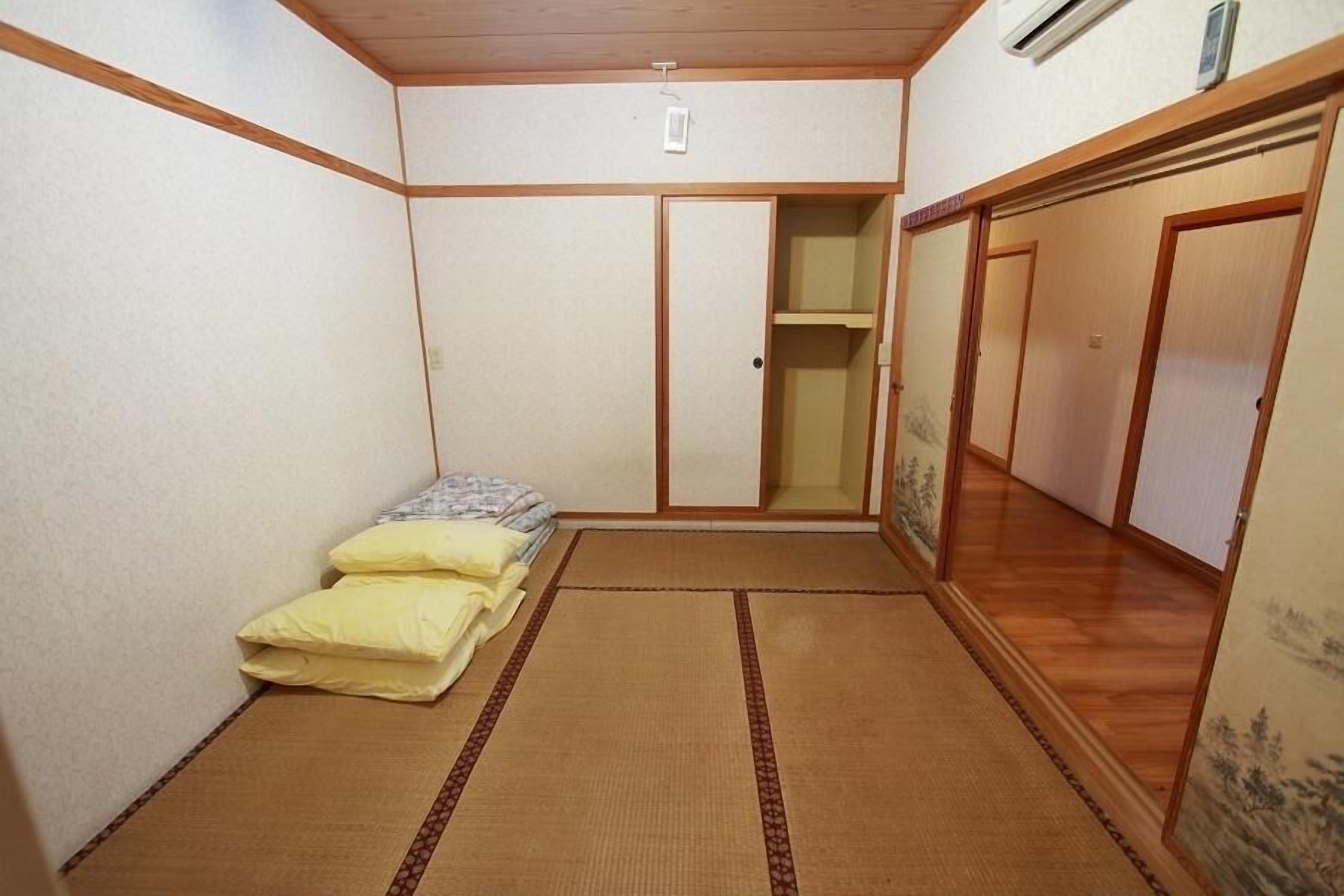 A traditional Japanese room with tatami flooring, a futon bed, sliding doors, and a small shelf.