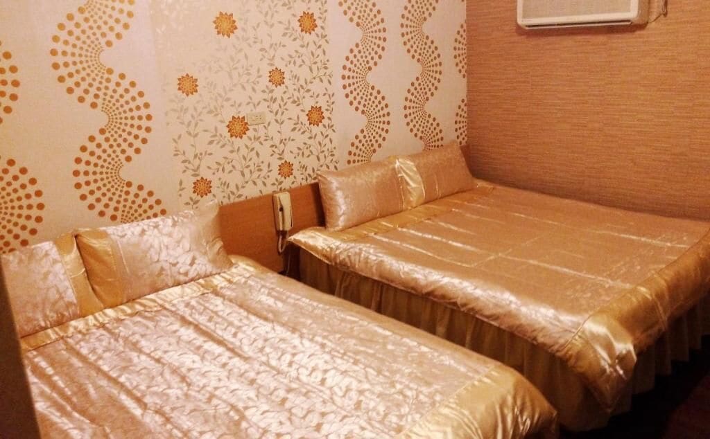 Una habitación con dos camas, cada una con una colcha dorada y almohadas a juego. Las paredes tienen un estampado de papel tapiz con motivos florales.