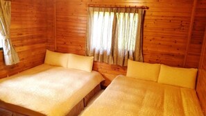 A wooden cabin room with two beds, a window with curtains, and a wooden ceiling.