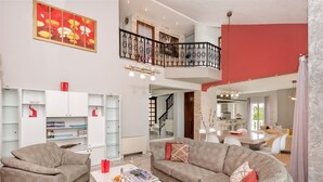 A spacious living area with a high ceiling, a balcony with a black railing, and a dining area with a modern table and chairs. - Grecian Villa Poseidon (Platanias)