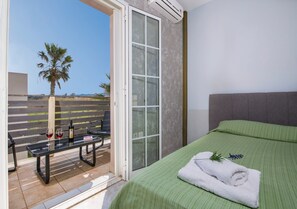 A bedroom with a green bedspread, a white towel, and a bottle of wine on a table by the sliding glass door. - Grecian Villa Poseidon (Platanias)