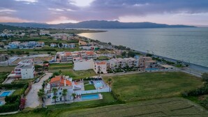 An aerial view of a coastal residential area with multiple apartment buildings, a swimming pool, and a road along the sea. - Grecian Villa Poseidon (Platanias)