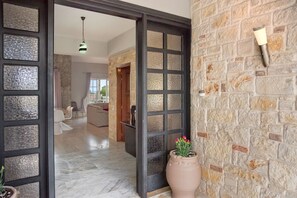 A hallway with a stone wall, a potted plant, and a door leading to a living area. - Grecian Villa Poseidon (Platanias)