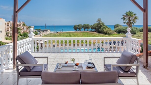 A covered outdoor seating area with a view of the sea, a pool, and greenery. - Grecian Villa Poseidon (Platanias)