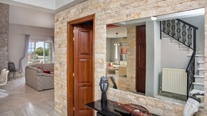 A modern living room with a stone wall, a wooden door, and a black table with a vase. - Grecian Villa Poseidon (Platanias)