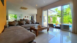 A spacious living room with a large sofa, a wooden coffee table, and a view of a swimming pool through large sliding glass doors.
