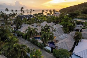 A residential area with multiple houses, some with sloped roofs, surrounded by lush greenery and palm trees.