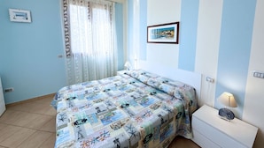 A bedroom with a bed, a nightstand, a lamp, a window with curtains, and a framed picture on the wall. - Appartamenti La Risacca - Appartamenti La Risacca - Trilo 4 VM (Capoliveri)