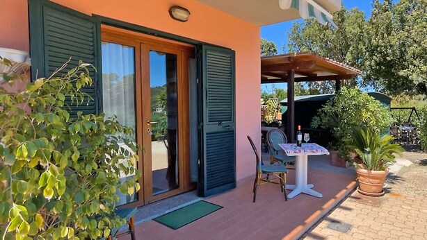 Ein Haus mit einer Terrasse, komplett mit Tisch, Stühlen, einem Blumentopf und einer Tür mit Fensterläden.
