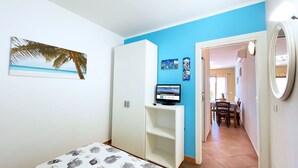 Ein Schlafzimmer mit Bett, Kleiderschrank, Schreibtisch mit Computer und Essbereich mit Stühlen und Tisch.