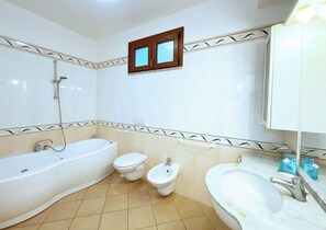 A bathroom with a bathtub, two toilets, a bidet, a sink, and a mirror.