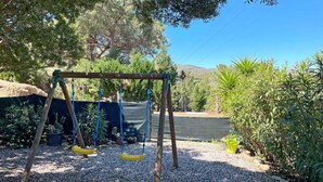 Un’altalena in legno con sedili gialli in un’area giardino con fondo in ghiaia, circondata da piante e alberi diversi.