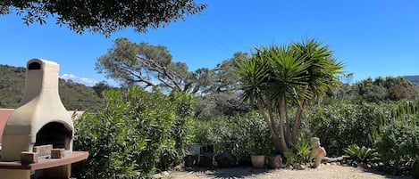 A rustic outdoor area with a stone oven, surrounded by gravel, trees, and a statue.