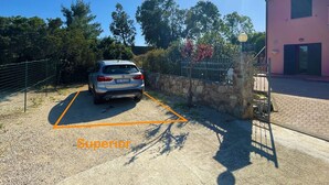 Un'area di parcheggio con un'auto, un muro in pietra, una recinzione metallica e un edificio con facciata rosa.