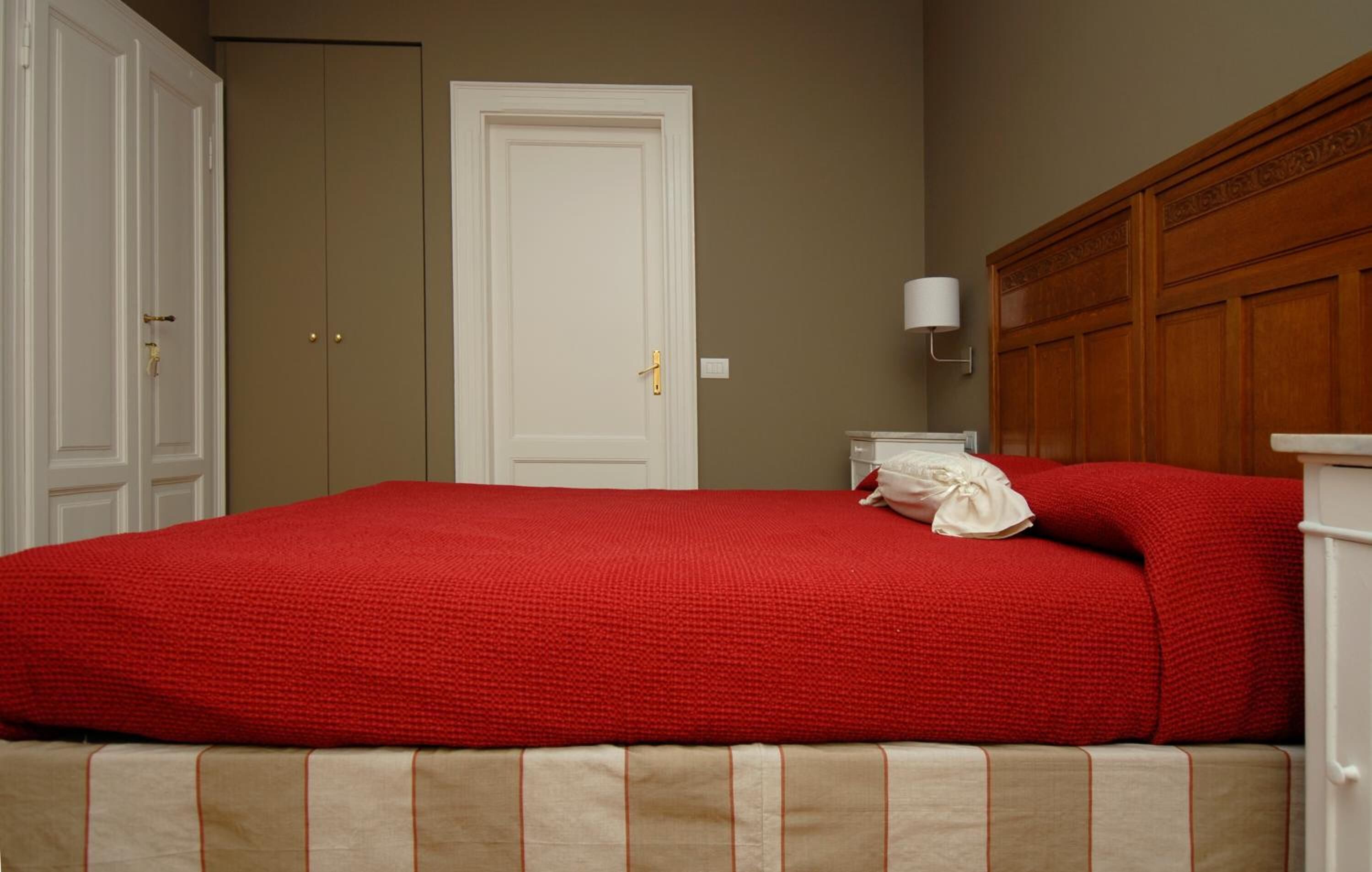 Une chambre à coucher avec une couvre-lit rouge, une tête de lit en bois, une table de chevet blanche avec une lampe et une porte fermée.