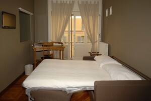 Un dormitorio con cama, un escritorio de madera, una silla, un radiador y una ventana con cortinas.