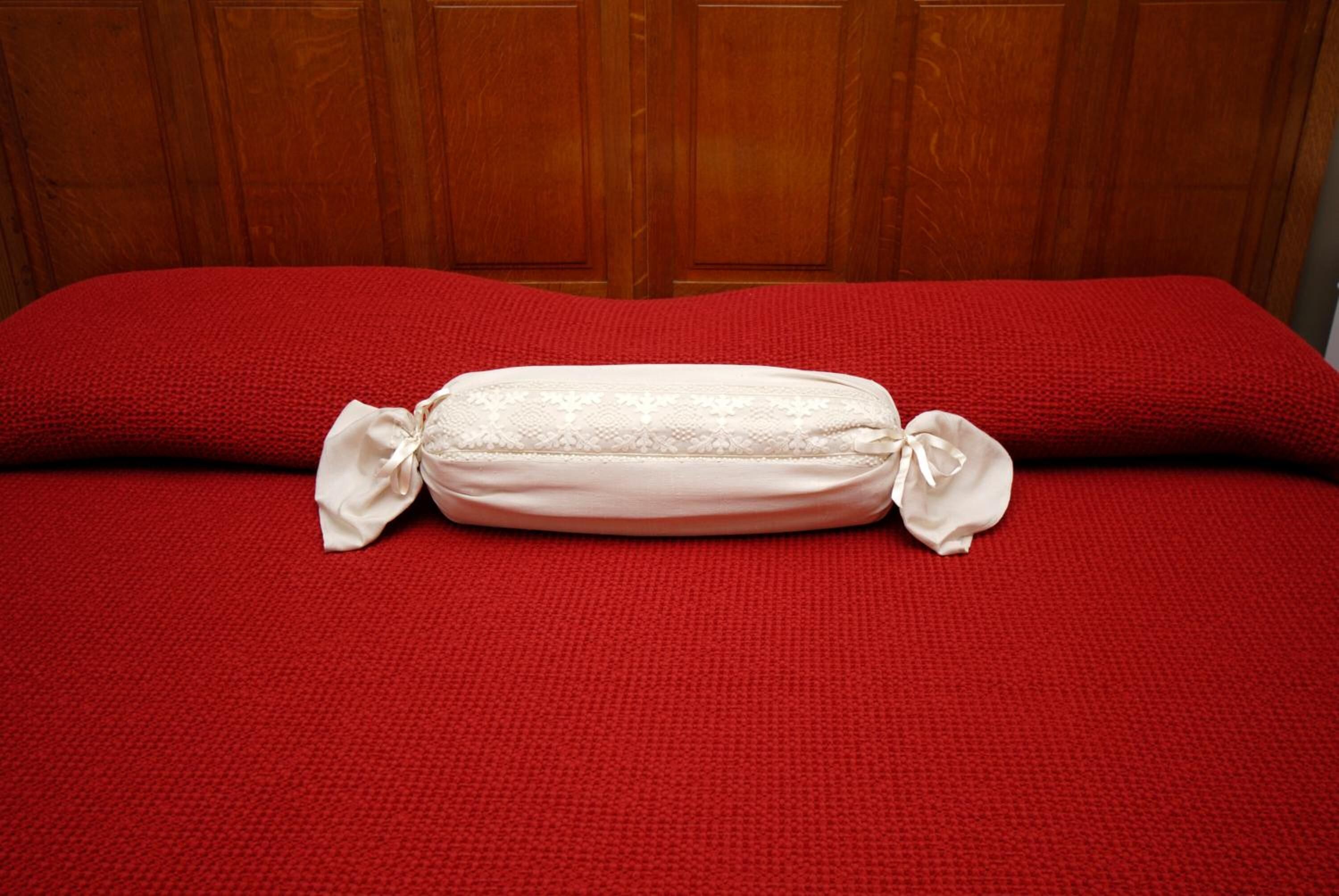 A bed with a red blanket and a white pillow with a bow.