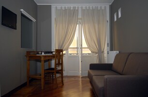 Una habitación con una mesa y sillas de madera, un sofá y un ventanal con cortinas.