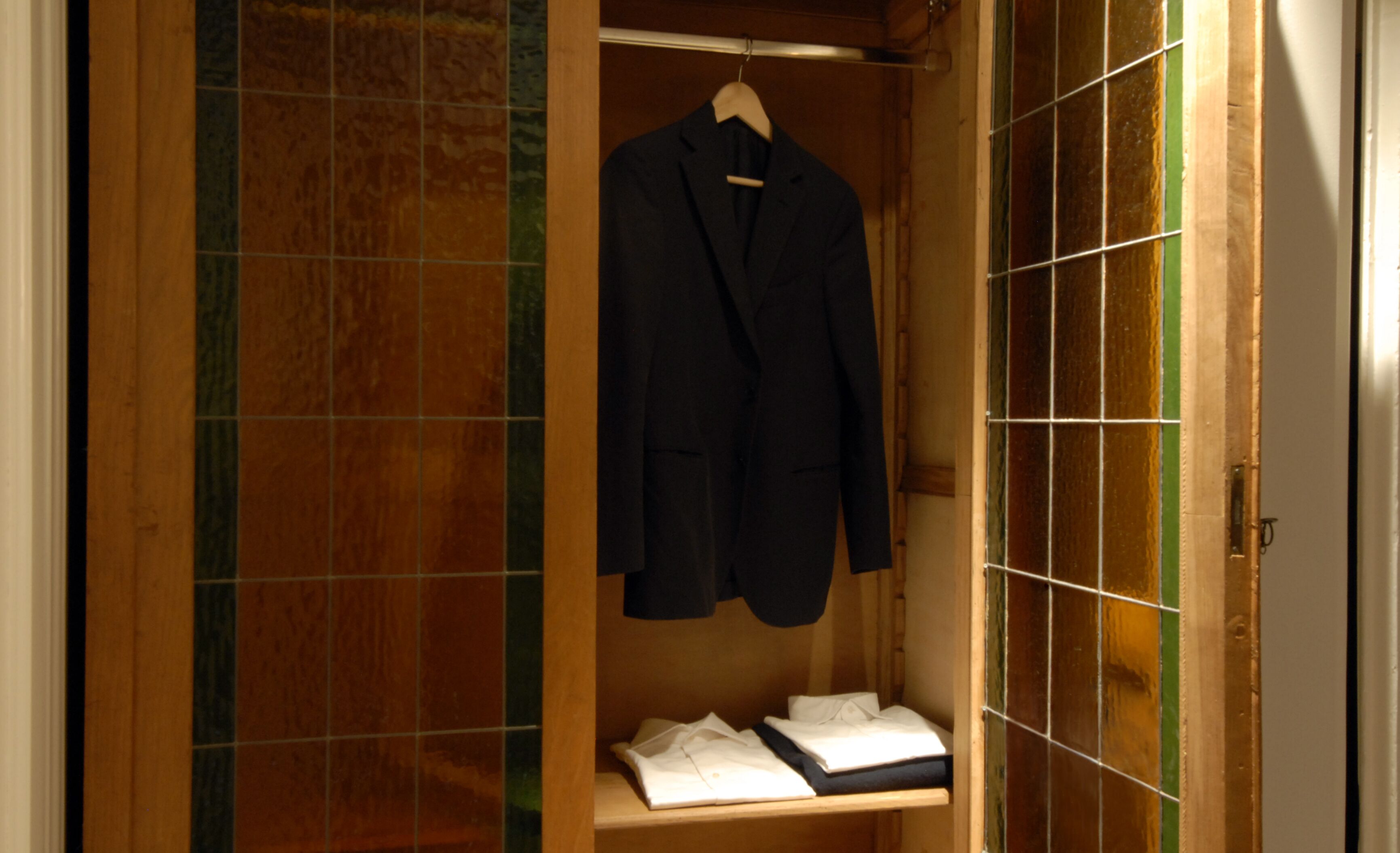 A wooden wardrobe with a hanging coat and neatly folded clothes inside.