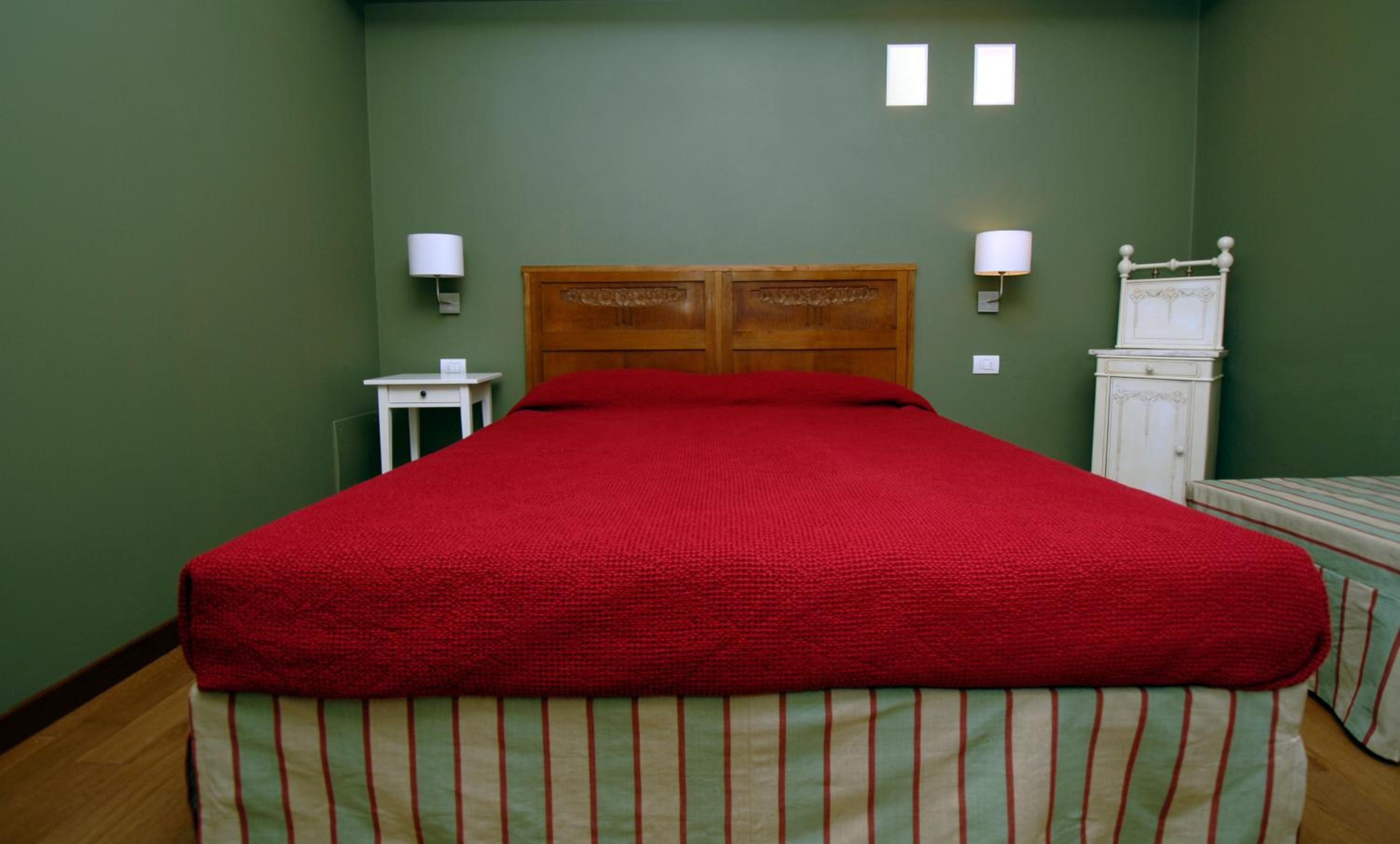 Una habitación con una cama grande, paredes verdes, dos lámparas de noche, una mesita pequeña y un aparador blanco.