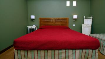 Una habitación con una cama grande, paredes verdes, dos lámparas de noche, una mesita pequeña y un aparador blanco.