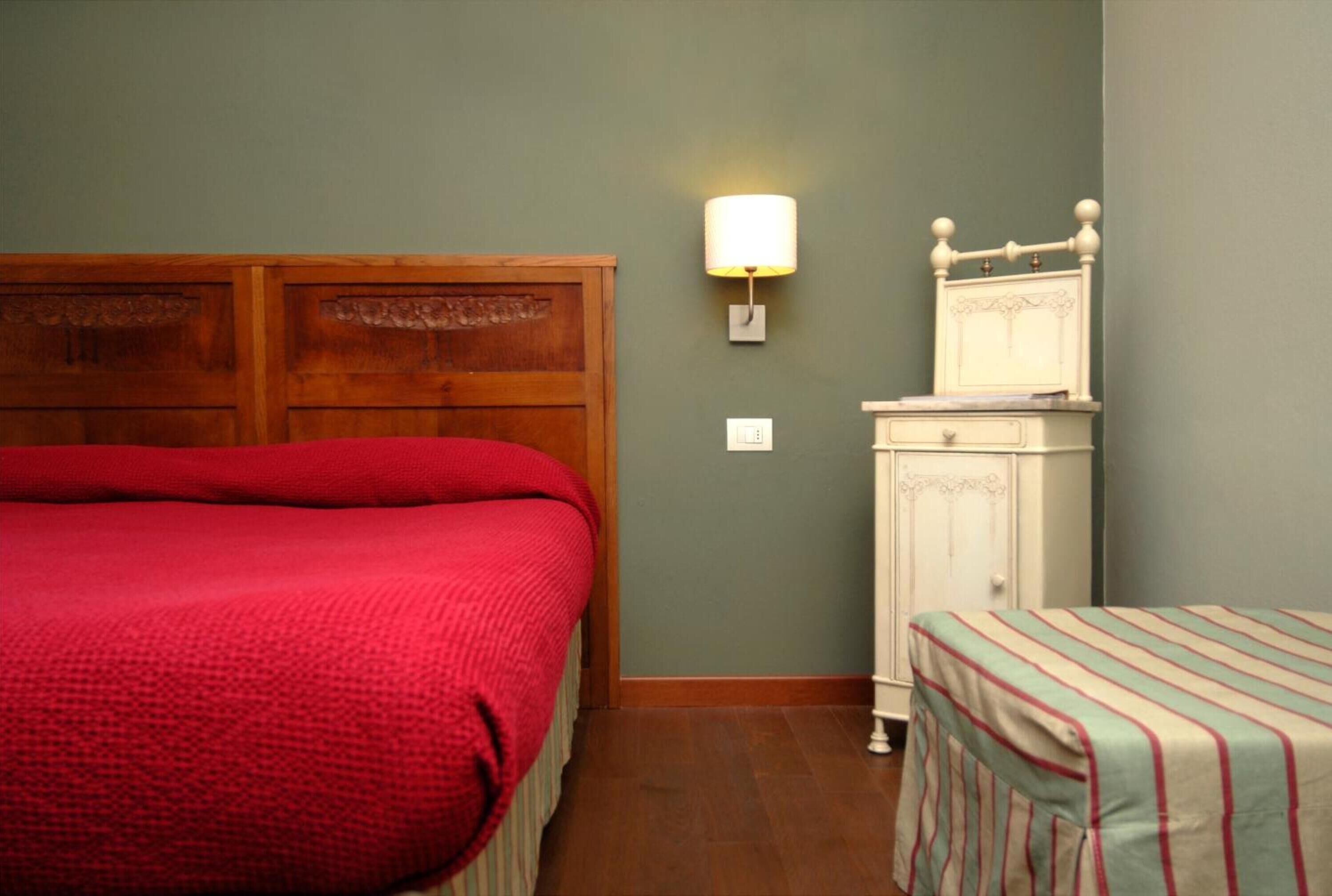 Una habitación con una cama de cabecera de madera, una mesita de noche con lámpara y un armario pequeño.