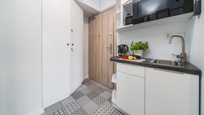 A compact kitchen with white cabinets, a black microwave, a sink, and a patterned floor. - Sarah Apartments Old Town (Kraków)