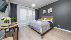 A modern bedroom with a bed, a small table with a vase of flowers, and a view of the outdoors. - Sarah Apartments Old Town (Kraków)