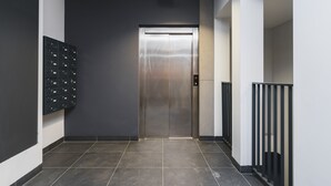 A modern elevator with a metallic finish, a wall-mounted storage unit with multiple compartments, and a tiled floor. - Sarah Apartments Old Town (Kraków)