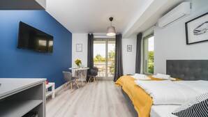 A modern hotel room with a bed, a desk, a chair, a small table with a vase of sunflowers, and a balcony with a view. - Sarah Apartments Old Town (Kraków)
