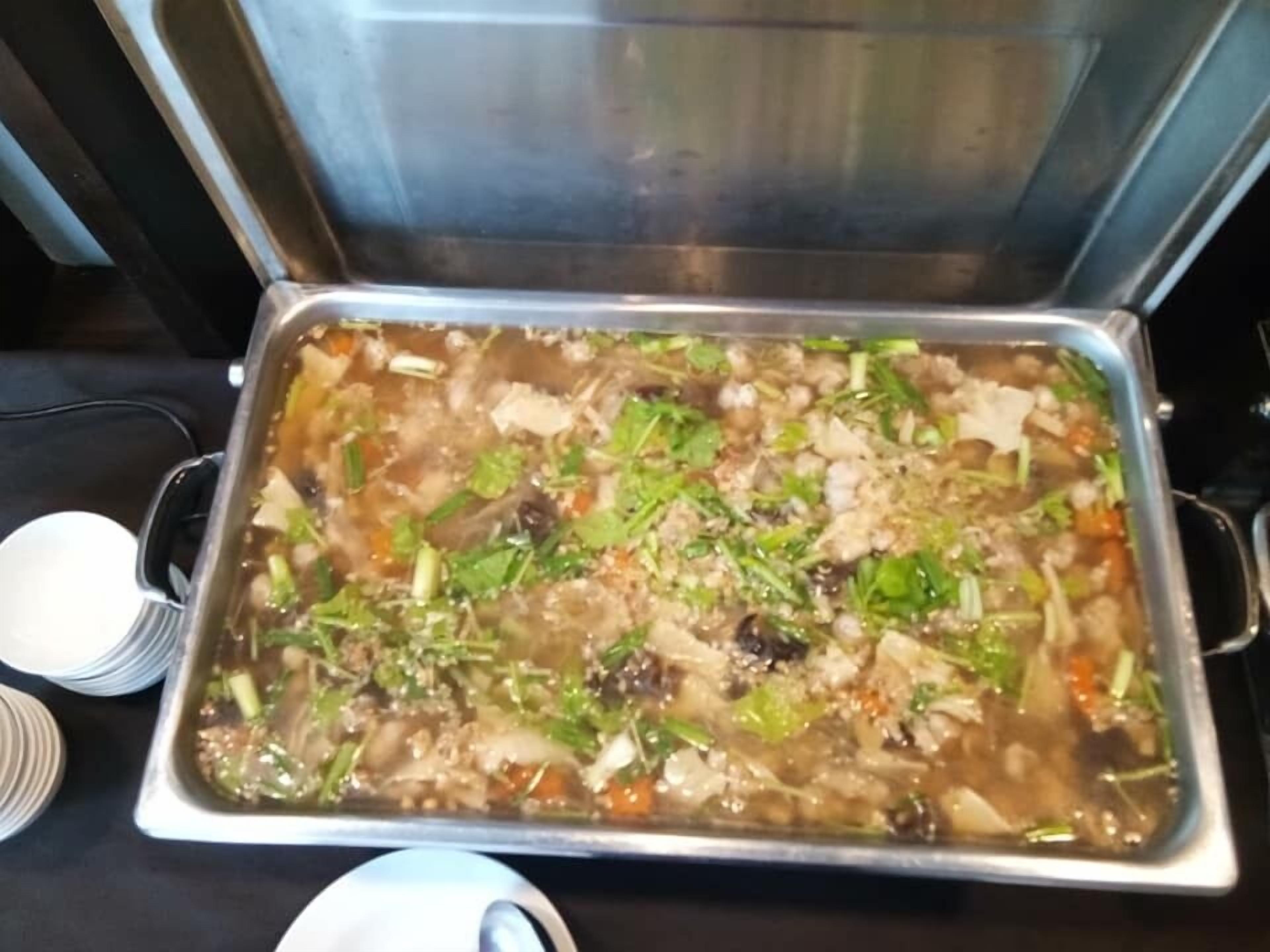 A buffet with a variety of dishes, including a large pot of soup with vegetables and meat.