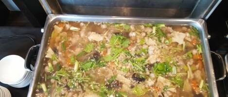A buffet with a variety of dishes, including a large pot of soup with vegetables and meat.