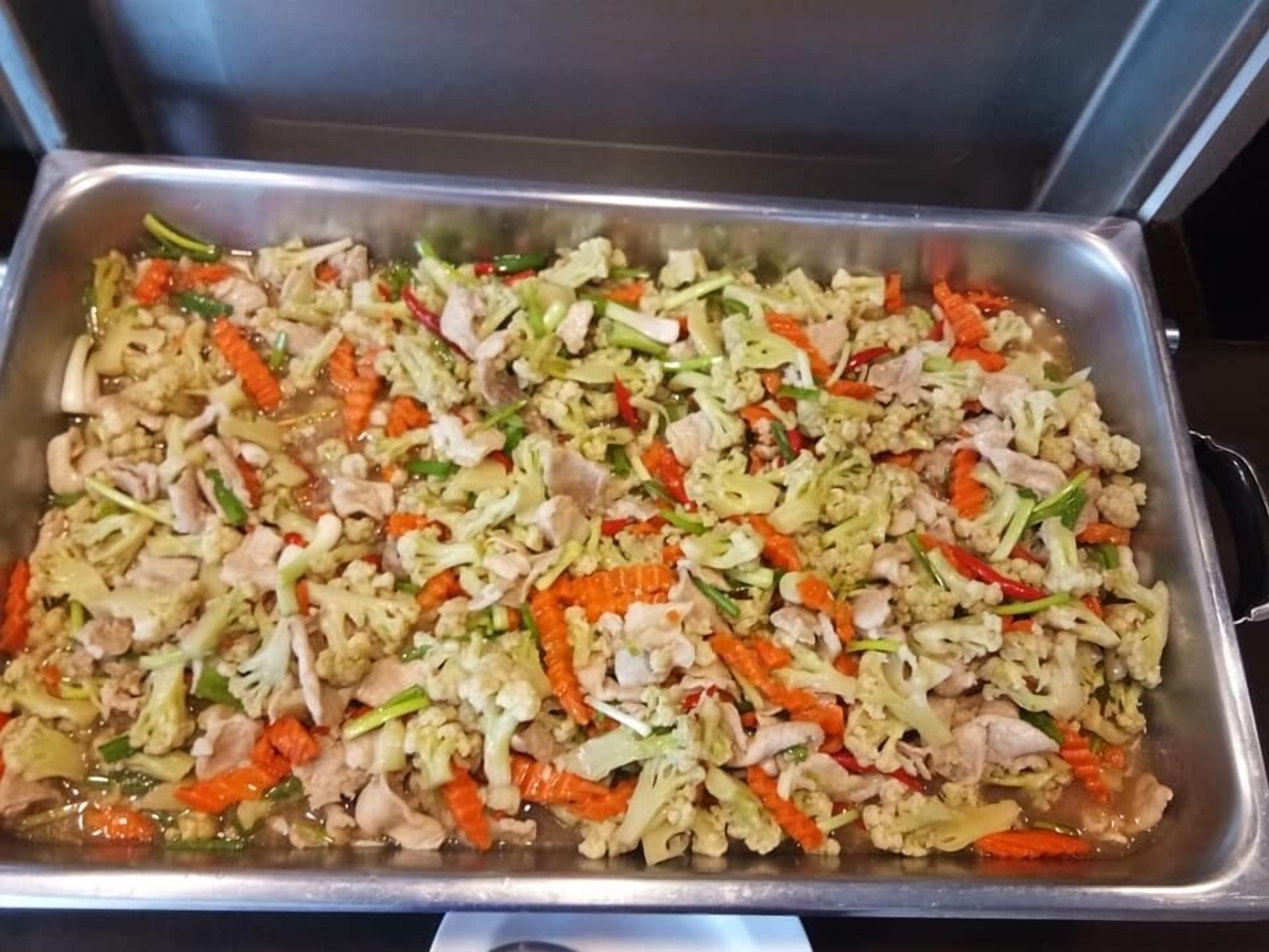Una bandeja de acero inoxidable llena de vegetales salteados y carne.