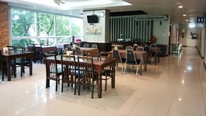 A spacious dining area with wooden tables and chairs, large windows, and a modern kitchen in the background. - KM Kwanphayao Hotel (Phayao)