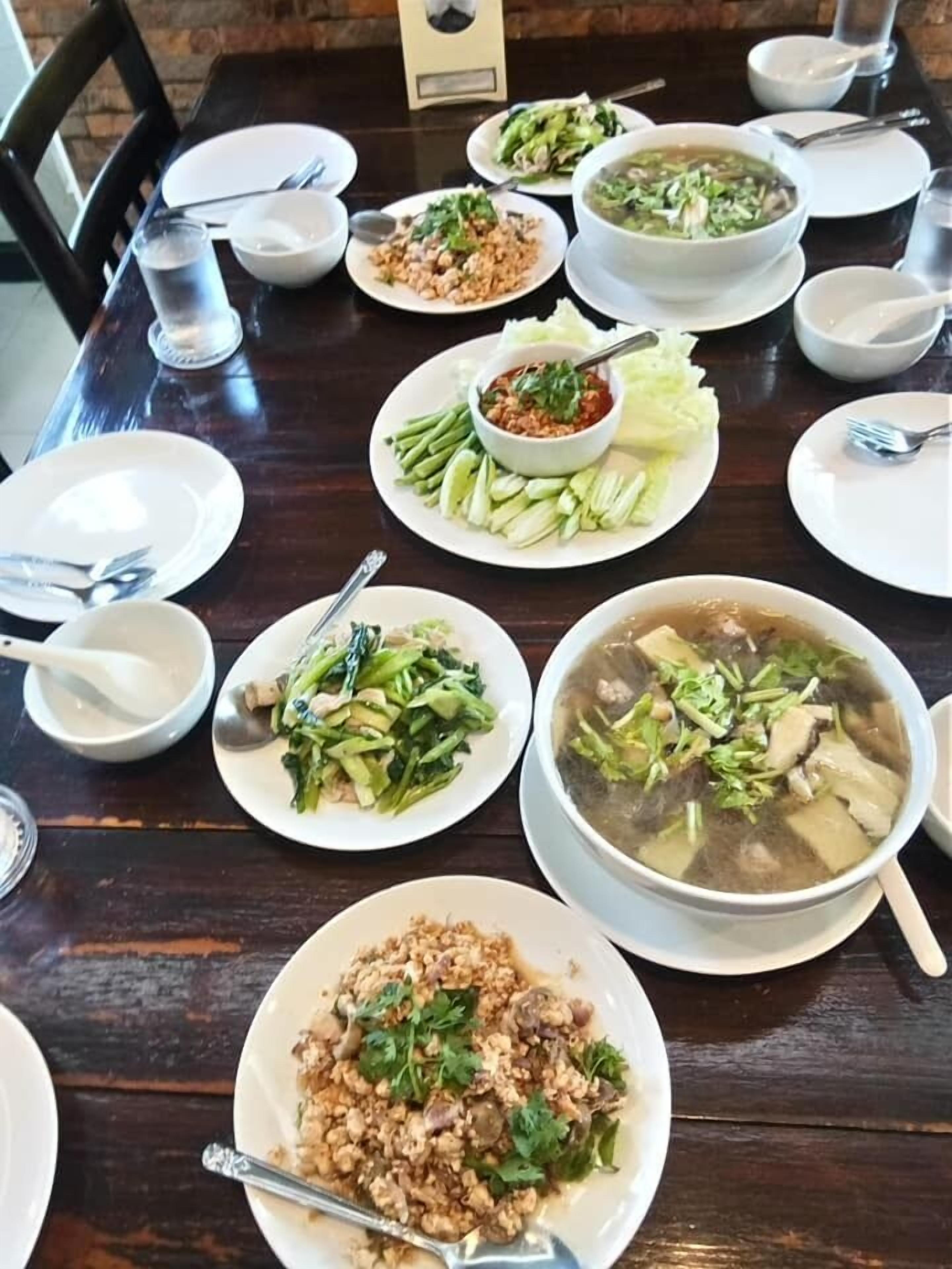 Una mesa de comedor dispuesta con varios platos, incluyendo un tazón grande de sopa, platos de vegetales salteados y un tazón de chile.