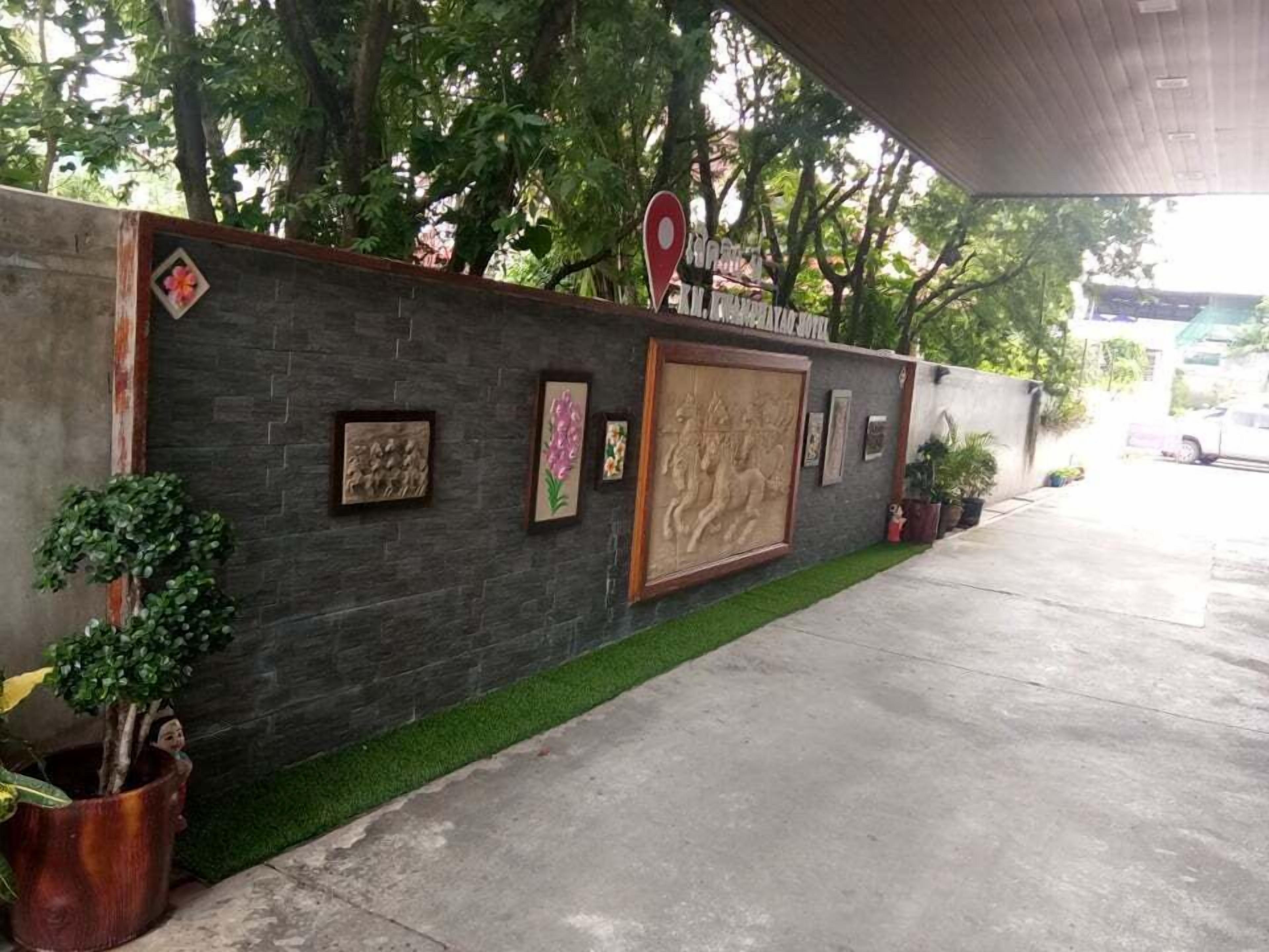 A hotel entrance with a dark stone wall, a red location pin sign, and various framed artworks.