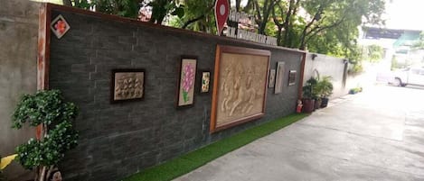 A hotel entrance with a dark stone wall, a red location pin sign, and various framed artworks.