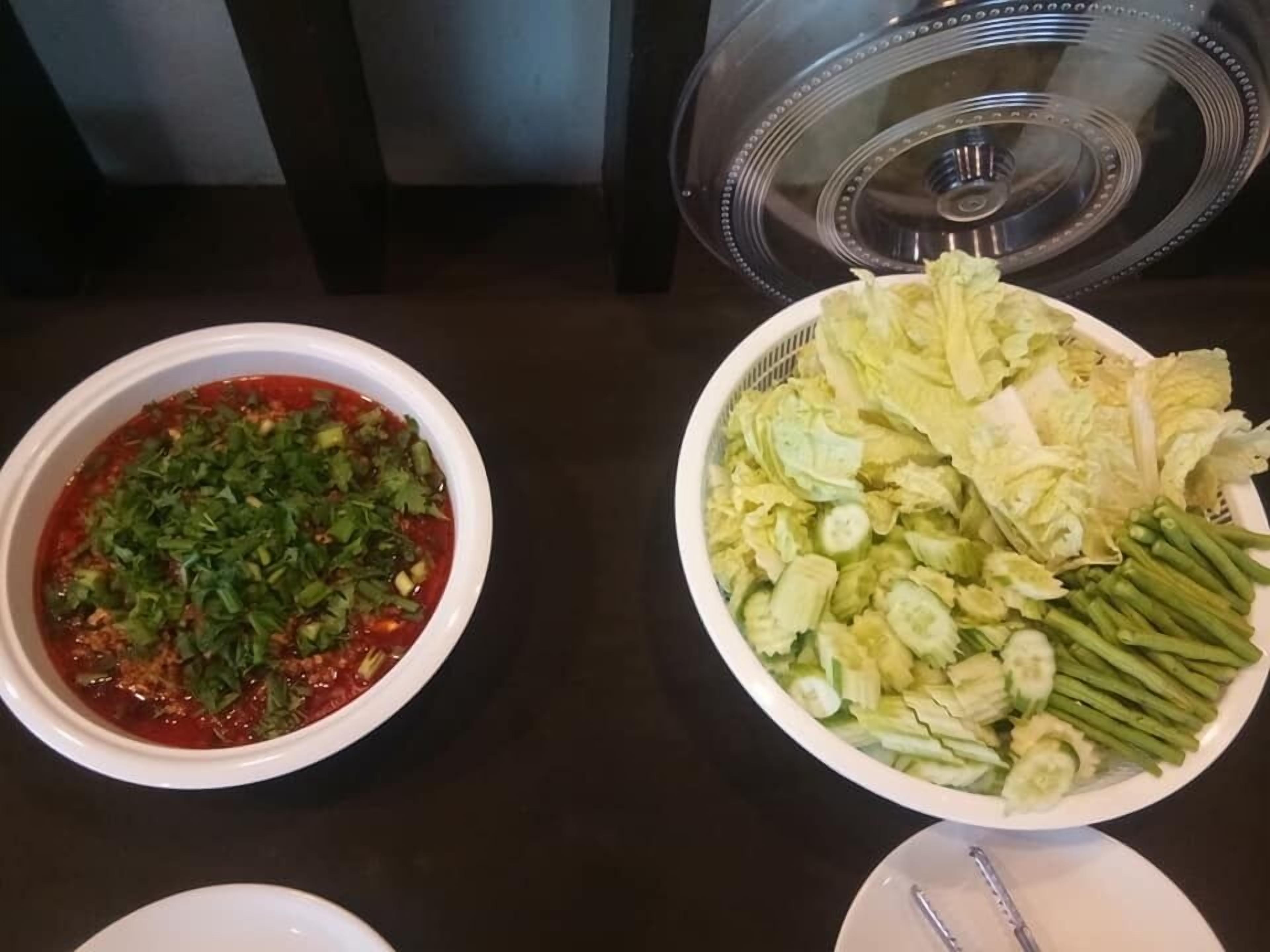 Una mesa con dos platos de comida, uno con salsa roja y hierbas picadas y el otro lleno de diferentes vegetales como lechuga, pepinos y judías verdes.